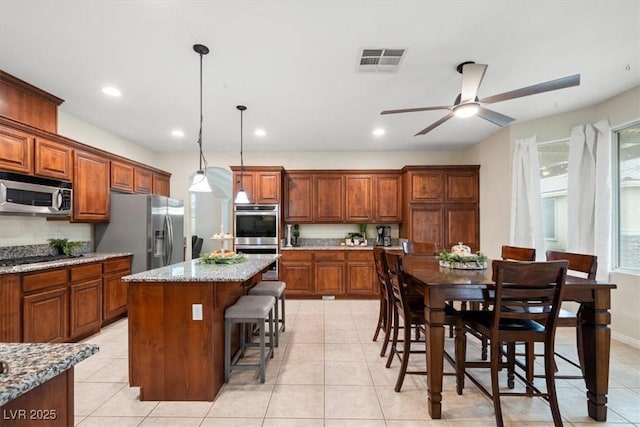 6335 Iginlas Goal Ave, Las Vegas, NV 89131 - kitchen with ceiling fan, brown cabinetry, stainless steel appliances, a kitchen island, and visible vents