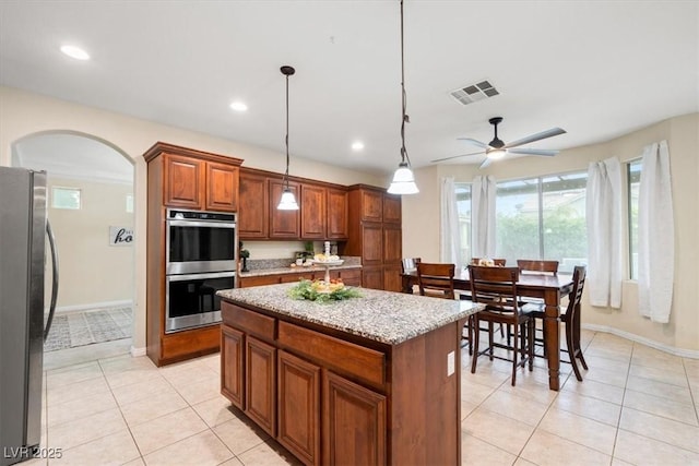 6335 Iginlas Goal Ave, Las Vegas, NV 89131 - kitchen featuring visible vents, a kitchen island, light stone counters, arched walkways, and stainless steel appliances