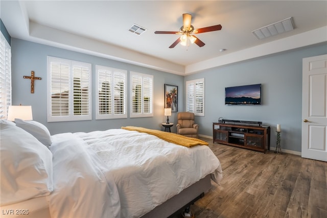 bedroom featuring baseboards, a tray ceiling, visible vents, and wood finished floors