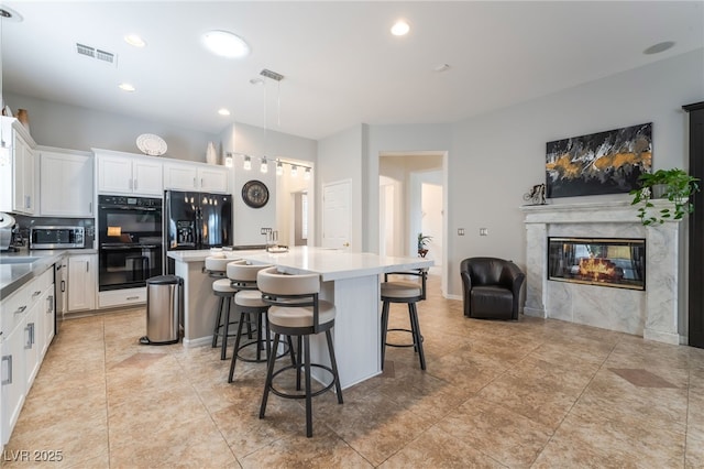 kitchen featuring white cabinets, a premium fireplace, visible vents, a center island with sink, and black appliances