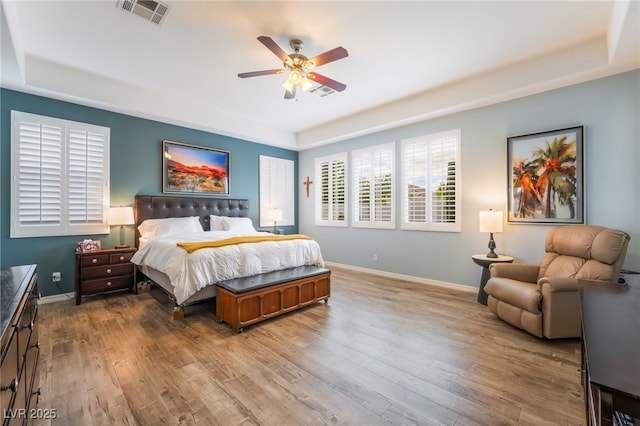bedroom with visible vents, baseboards, wood finished floors, and a tray ceiling