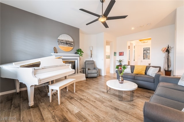 living area featuring a glass covered fireplace, a ceiling fan, and wood finished floors