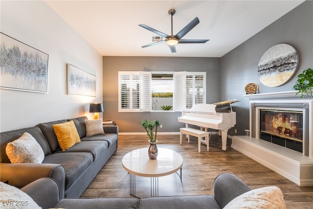 living room with a glass covered fireplace, baseboards, ceiling fan, and wood finished floors