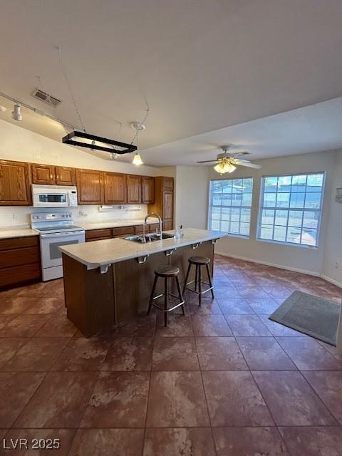 7650 Butterscotch Ct, Las Vegas, NV 89131 - kitchen with white appliances, brown cabinetry, a breakfast bar area, light countertops, and a center island with sink