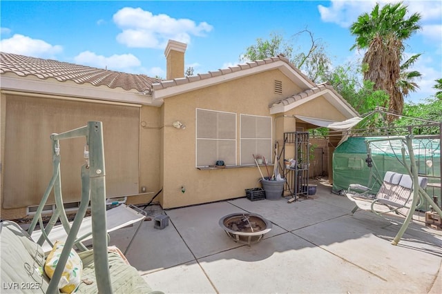 rear view of house with stucco siding, a chimney, a patio, a tiled roof, and a fire pit