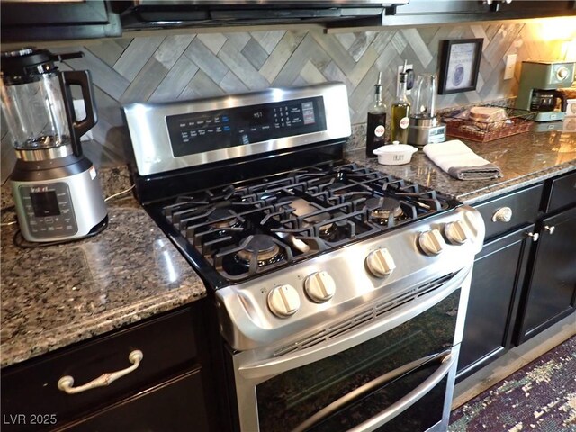 4361 Duck Harbor Ave, North Las Vegas, NV 89031 - kitchen featuring dark stone counters, dark cabinetry, tasteful backsplash, and range with two ovens