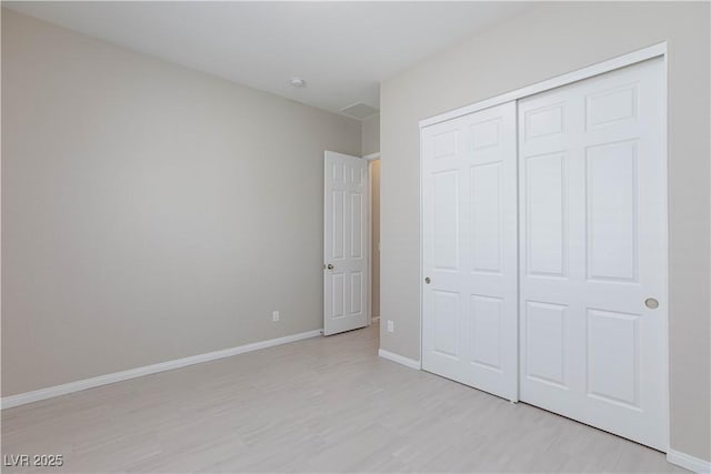 unfurnished bedroom featuring baseboards, light wood-style flooring, and a closet