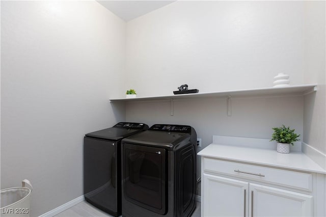 clothes washing area featuring washing machine and clothes dryer, baseboards, and cabinet space