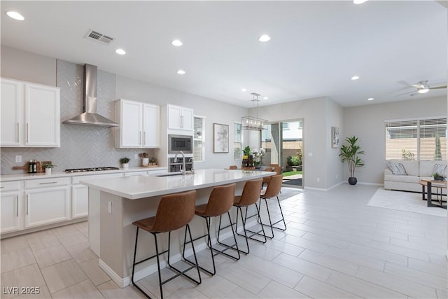 kitchen with visible vents, gas cooktop, wall chimney exhaust hood, stainless steel microwave, and a sink