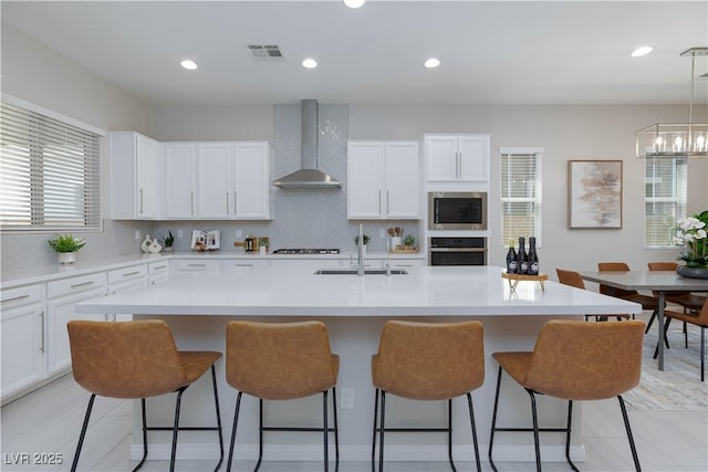 kitchen featuring wall chimney range hood, appliances with stainless steel finishes, a sink, a breakfast bar area, and visible vents