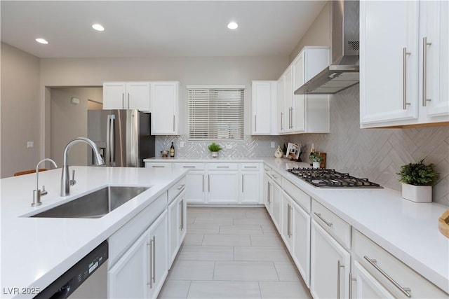 kitchen with stainless steel appliances, white cabinetry, a sink, and wall chimney exhaust hood
