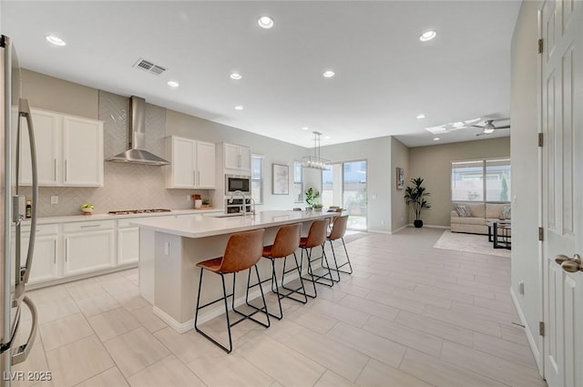 10251 Tiger Milkweed St, Las Vegas, NV 89141 - kitchen with wall chimney exhaust hood, tasteful backsplash, a breakfast bar area, a kitchen island with sink, and white cabinetry