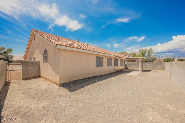 view of side of home featuring a fenced backyard, a patio, stucco siding, and a tiled roof