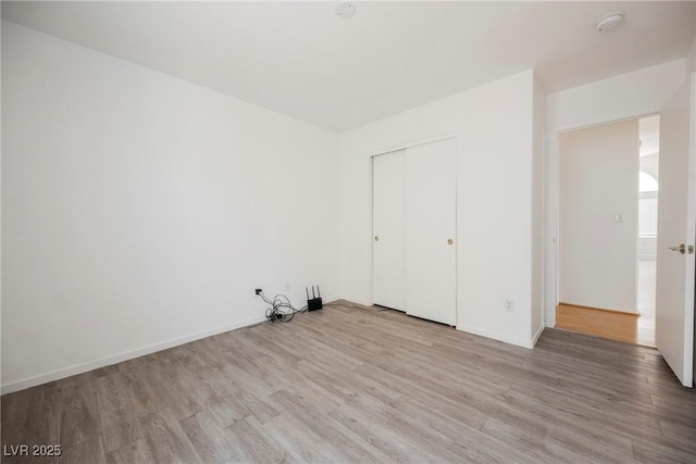 unfurnished bedroom featuring baseboards, wood finished floors, and a closet