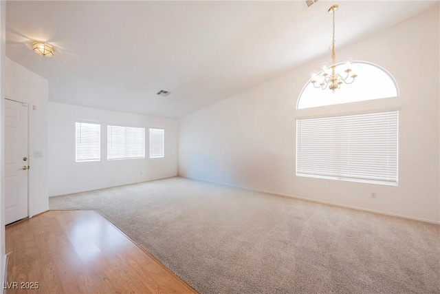 interior space featuring an inviting chandelier, vaulted ceiling, carpet flooring, and wood finished floors