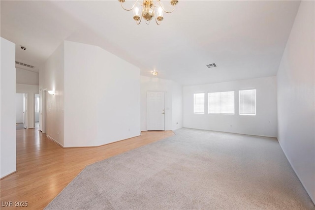 unfurnished room with visible vents, vaulted ceiling, wood finished floors, and a notable chandelier