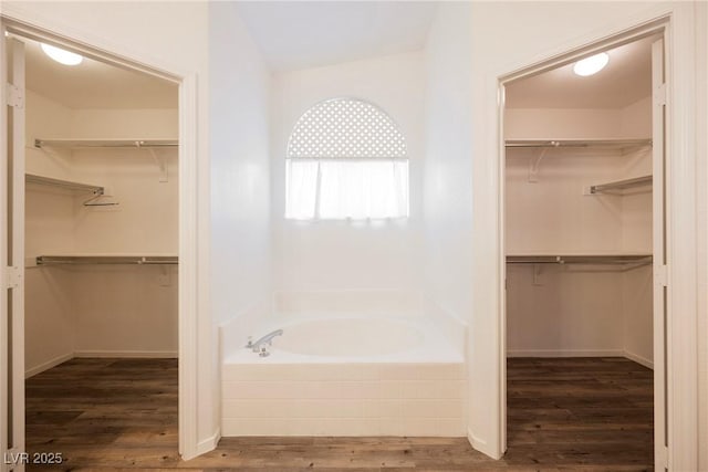 bathroom featuring a spacious closet, wood finished floors, and a bath
