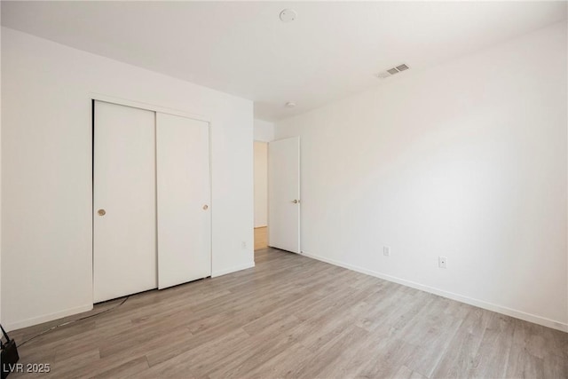 unfurnished bedroom featuring baseboards, a closet, light wood-type flooring, and visible vents