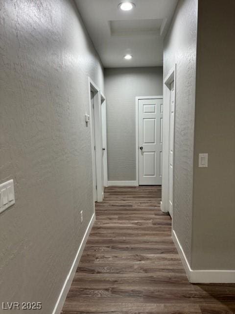 hall featuring baseboards, attic access, dark wood finished floors, and a textured wall