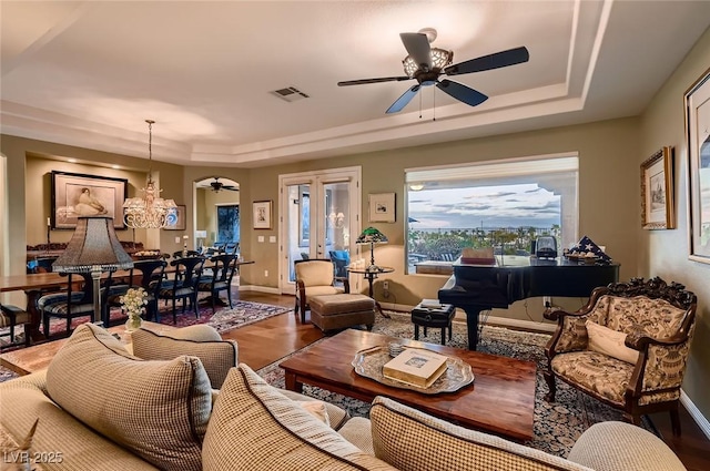 living room with a ceiling fan, a tray ceiling, visible vents, and wood finished floors