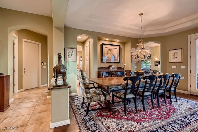 dining area featuring light tile patterned floors, arched walkways, a raised ceiling, and a notable chandelier