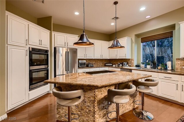 kitchen with a sink, a kitchen island, multiple ovens, white cabinetry, and cooktop