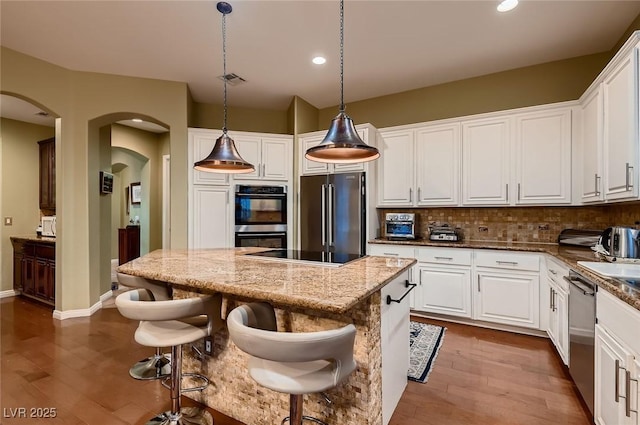 kitchen featuring appliances with stainless steel finishes, a center island, arched walkways, wood finished floors, and white cabinets