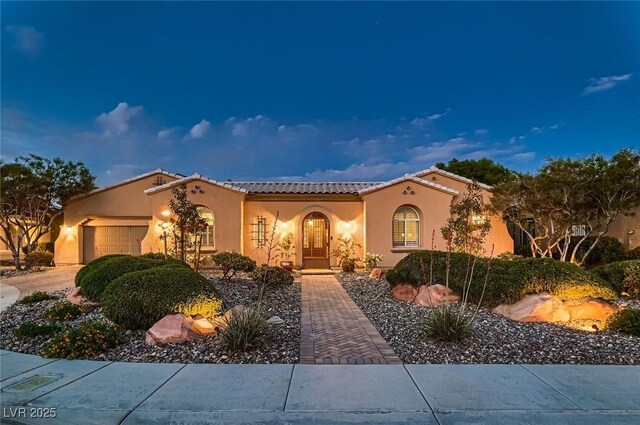 mediterranean / spanish home featuring a garage, stucco siding, a tile roof, and concrete driveway