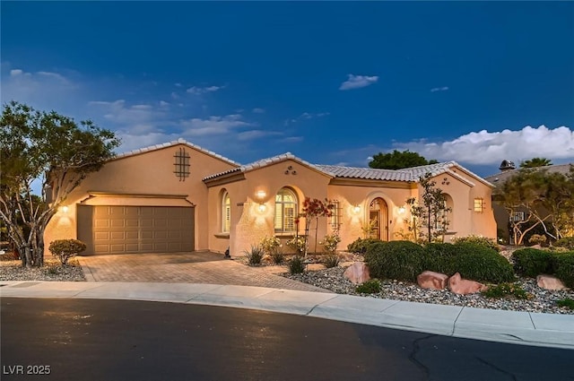mediterranean / spanish home with decorative driveway, an attached garage, a tile roof, and stucco siding