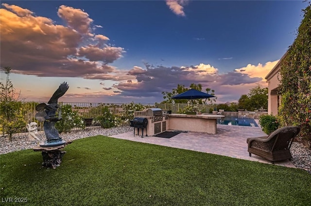 yard at dusk featuring an outdoor kitchen, a fenced backyard, and a patio area