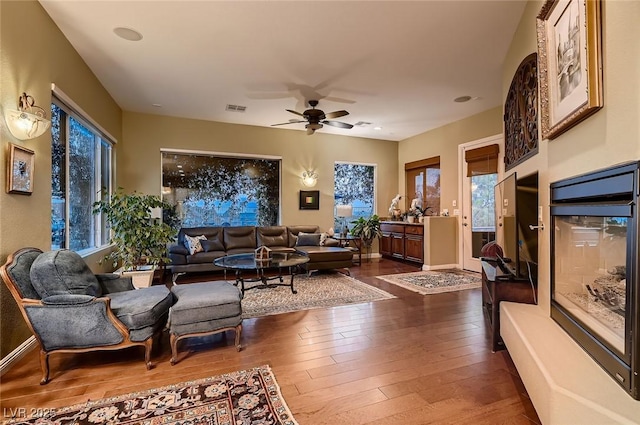 living area with plenty of natural light, a ceiling fan, visible vents, and dark wood-type flooring