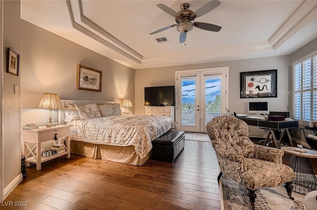 bedroom with ceiling fan, visible vents, a raised ceiling, access to outside, and hardwood / wood-style floors