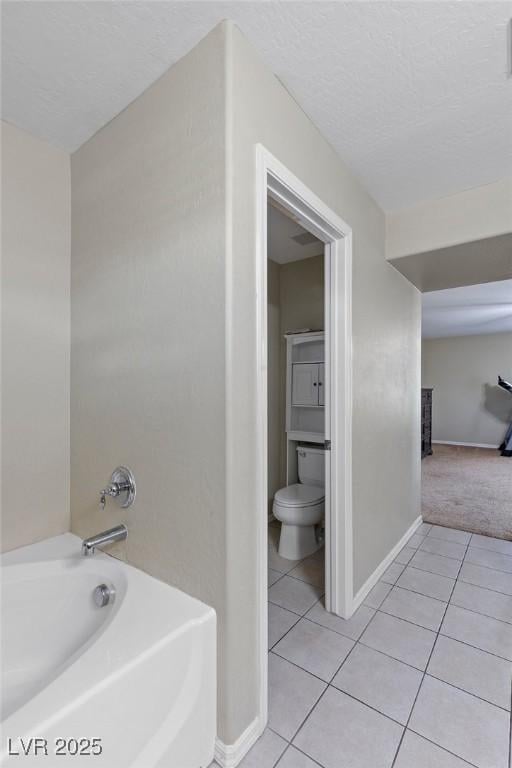 bathroom with baseboards, a bath, tile patterned floors, and toilet