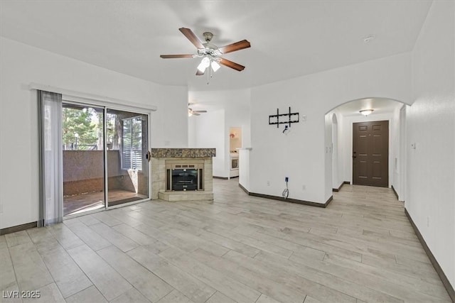 unfurnished living room featuring arched walkways, baseboards, a ceiling fan, and light wood finished floors