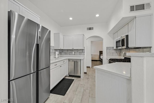 kitchen featuring visible vents, arched walkways, white cabinetry, and stainless steel appliances
