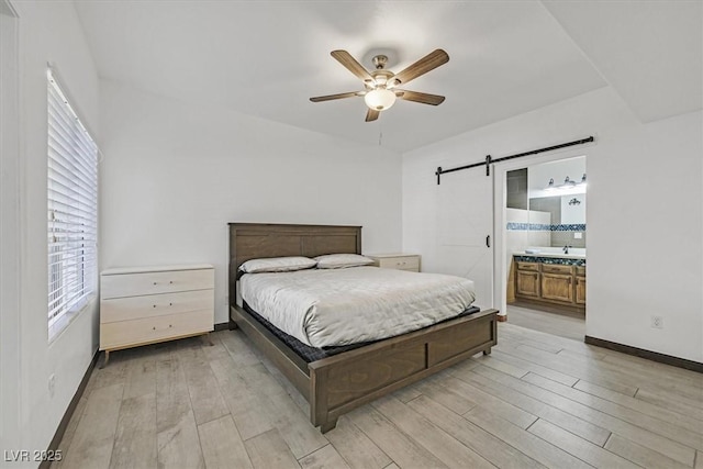 bedroom with baseboards, a barn door, light wood-style flooring, and connected bathroom
