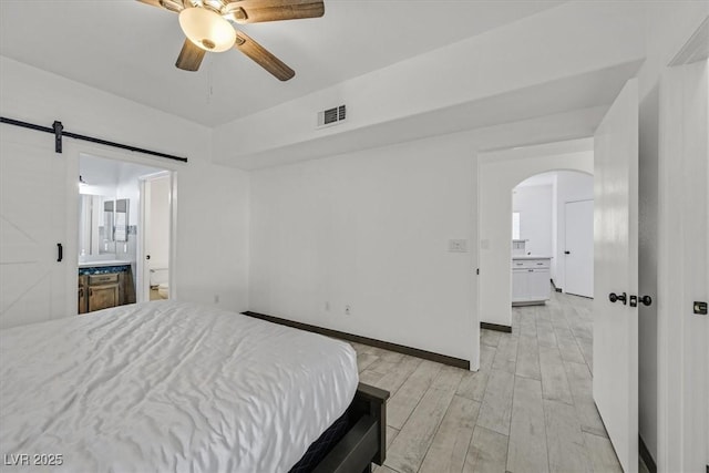 bedroom featuring visible vents, arched walkways, light wood-type flooring, a barn door, and connected bathroom