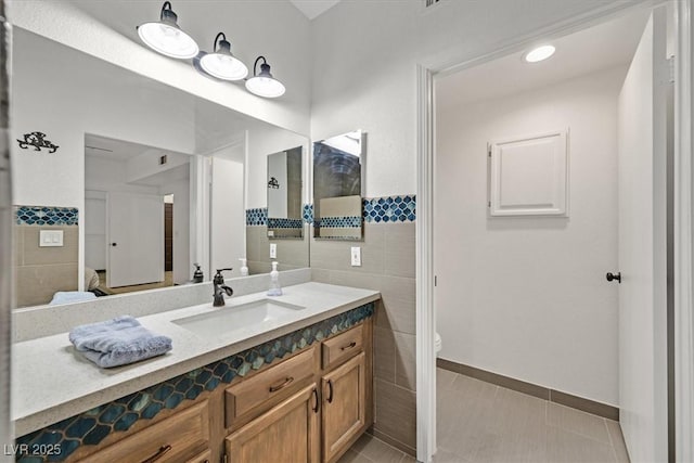 bathroom featuring vanity, toilet, tile patterned floors, a wainscoted wall, and tile walls