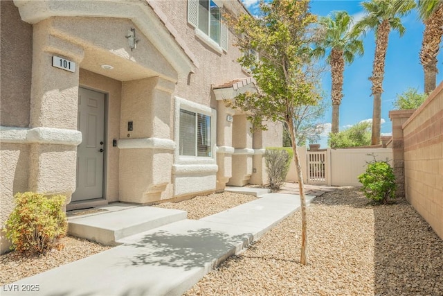 property entrance featuring fence, a gate, and stucco siding