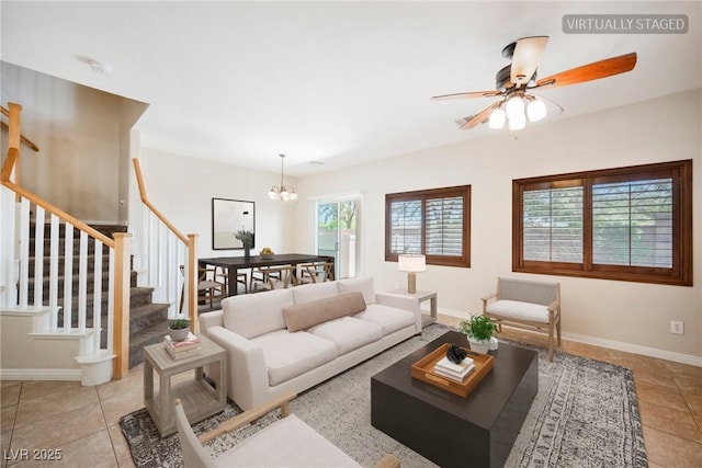 living room featuring tile patterned floors, baseboards, ceiling fan with notable chandelier, and stairs