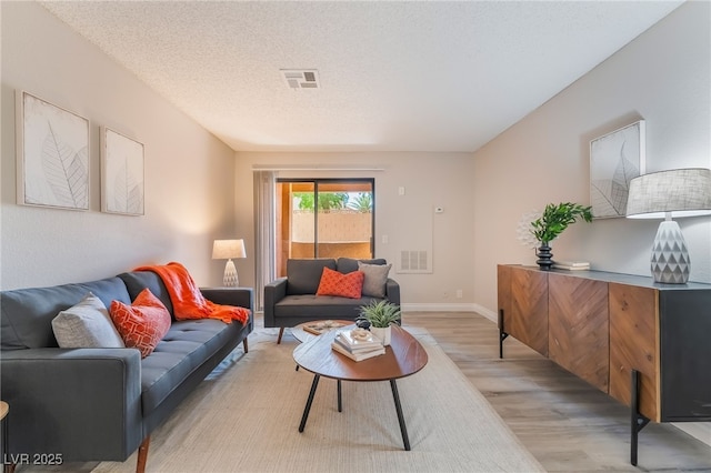 living room featuring light wood-style floors, a textured ceiling, baseboards, and visible vents