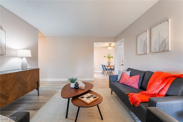 living area featuring a textured ceiling, baseboards, and light wood-type flooring