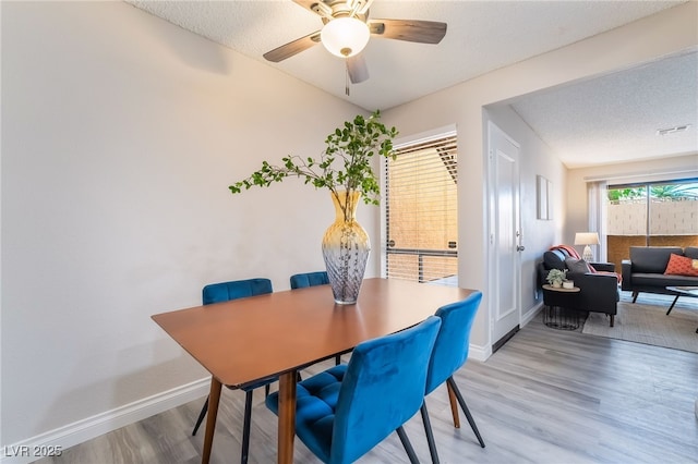 dining area featuring a textured ceiling, a ceiling fan, baseboards, wood finished floors, and visible vents
