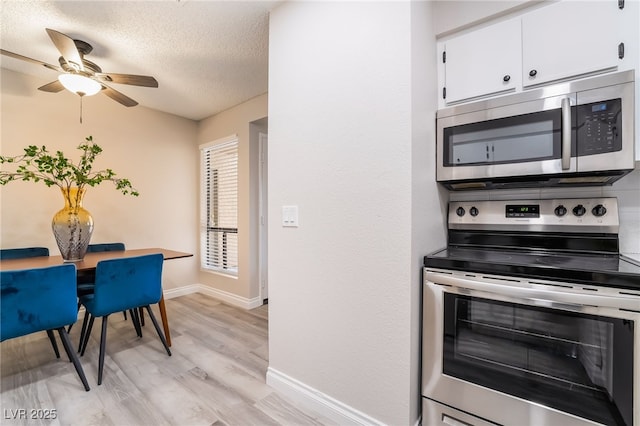 kitchen with baseboards, white cabinetry, a ceiling fan, light wood finished floors, and stainless steel appliances