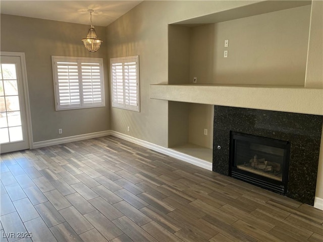 unfurnished living room with baseboards, a notable chandelier, a healthy amount of sunlight, and wood finished floors