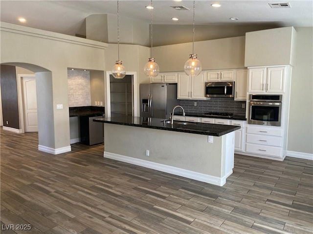 kitchen with stainless steel appliances, arched walkways, white cabinetry, and baseboards