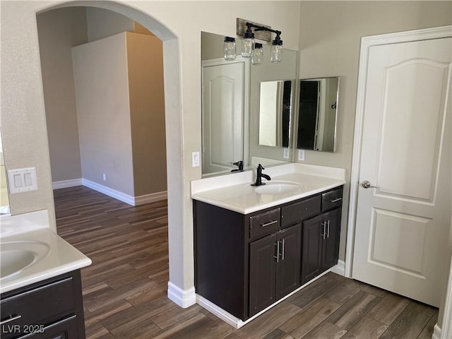full bathroom with baseboards, a sink, wood finished floors, and two vanities