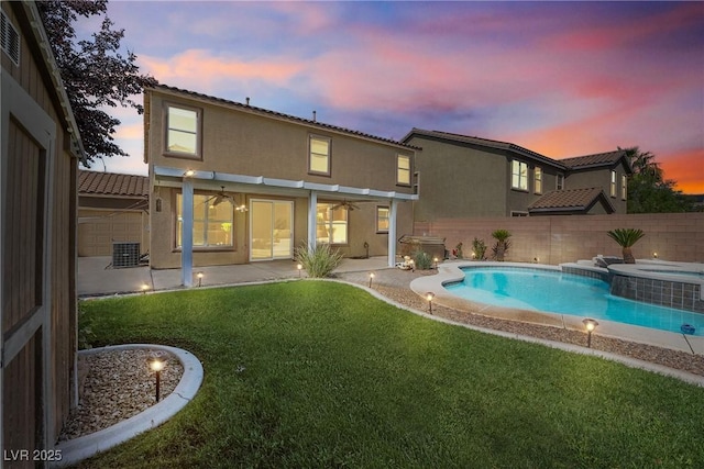 248 Hyssop Ct, Henderson, NV 89015 - back of house at dusk with a fenced backyard, stucco siding, a patio area, a lawn, and a pool with connected hot tub