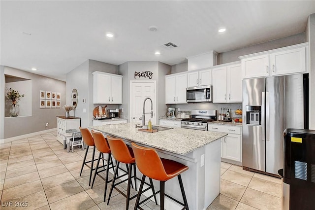 kitchen with appliances with stainless steel finishes, a sink, a kitchen island with sink, light tile patterned floors, and visible vents