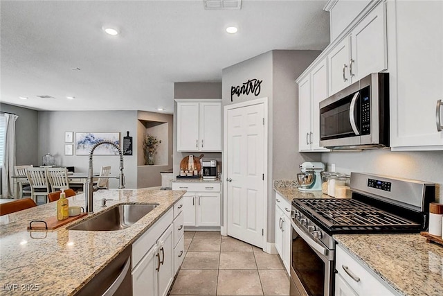 kitchen with white cabinetry, light stone counters, a sink, appliances with stainless steel finishes, and light tile patterned floors